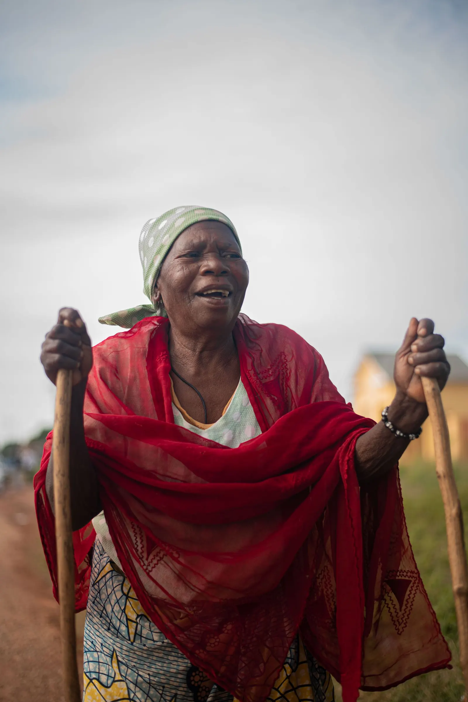 Smiling older African woman in a red shawl walking with the support of two sticks