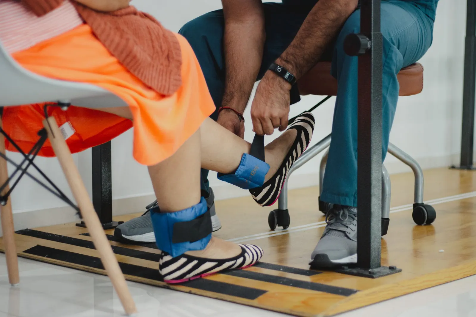 Physiotherapist fitting ankle weights on a patient's legs during a rehab session